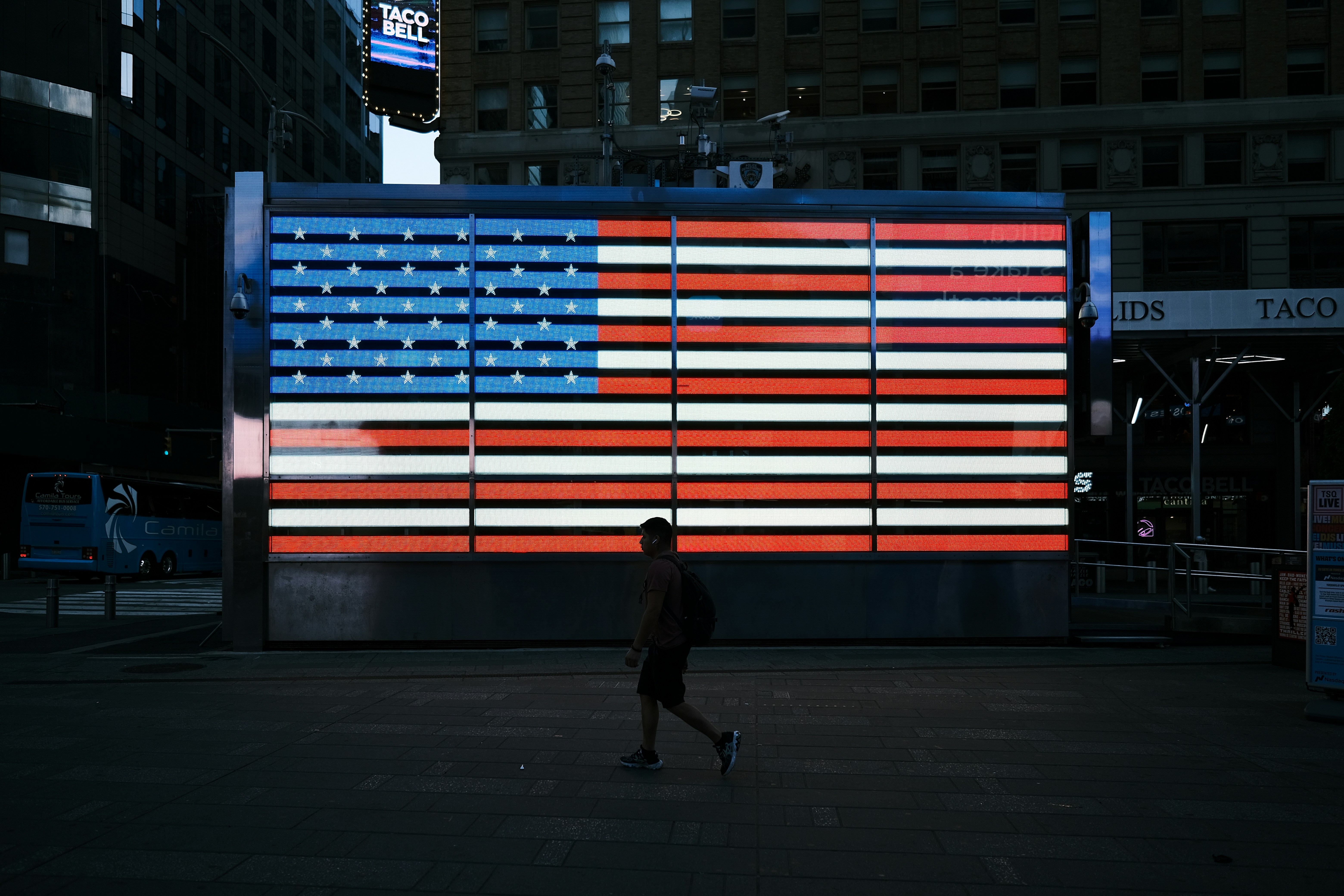 A man walking past a large american flag projected on a wall