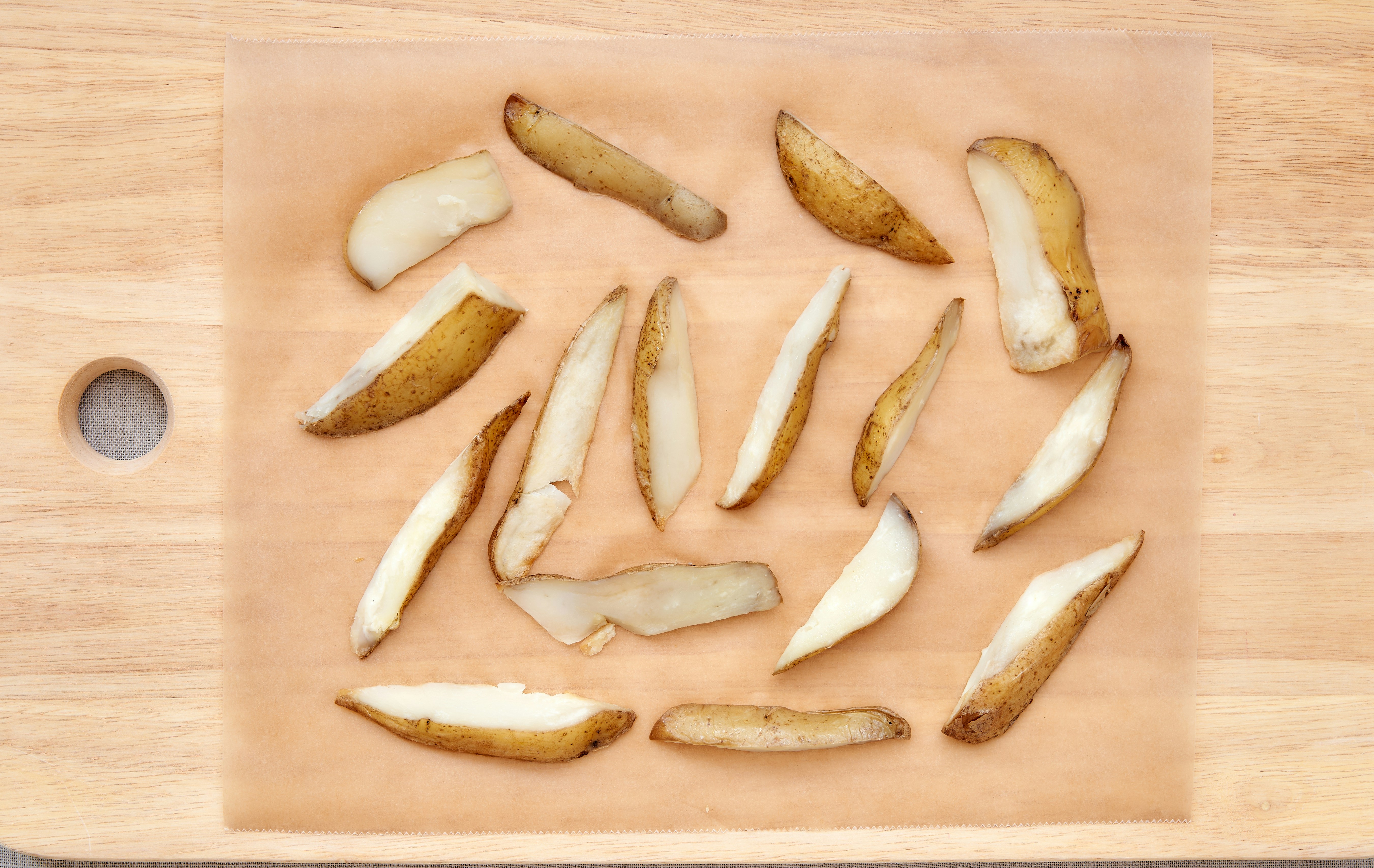 A wooden cutting board topped with sliced potatoes