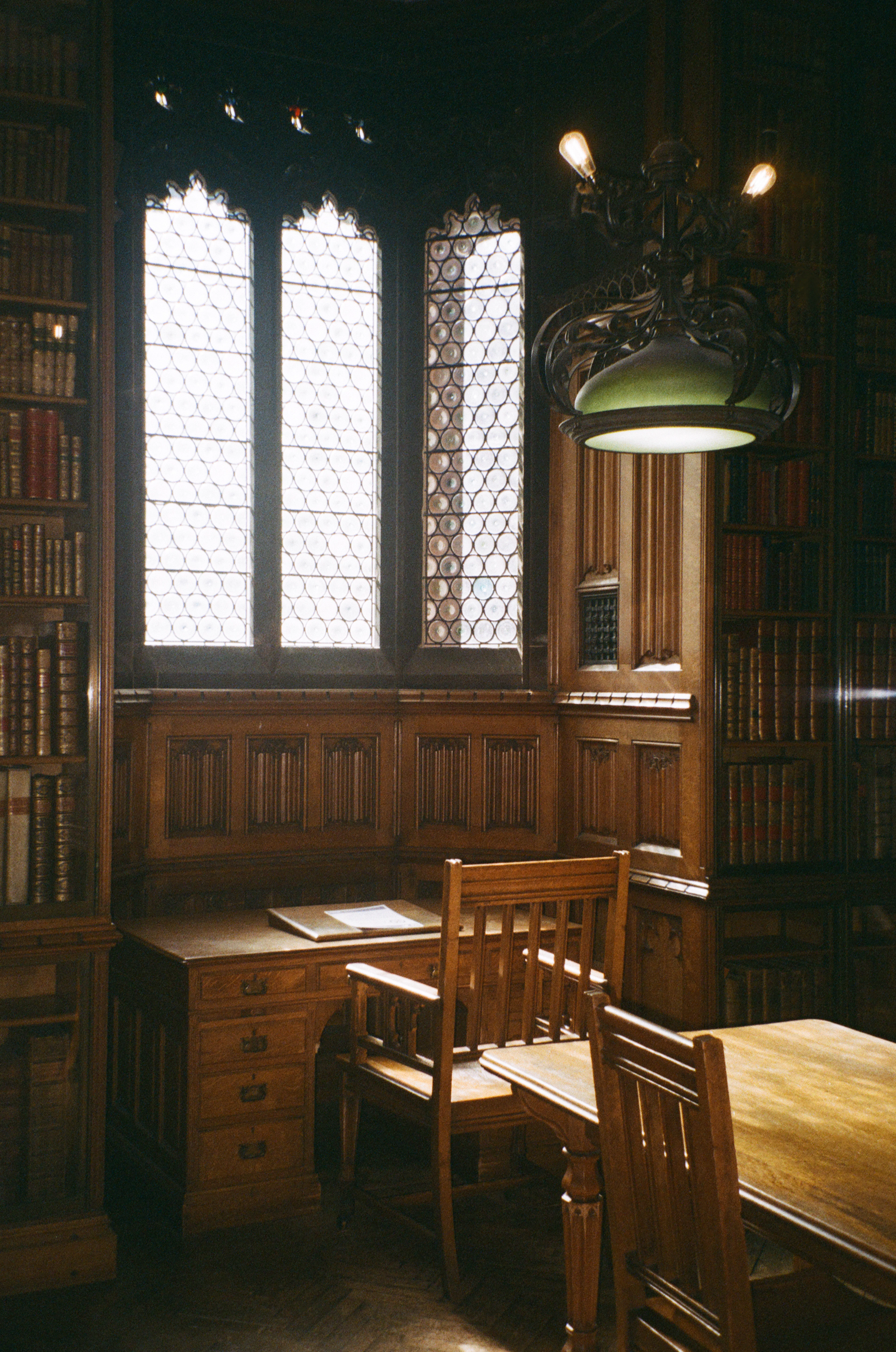 Wood-paneled library reading room with Gothic stained-glass windows and hanging lamps