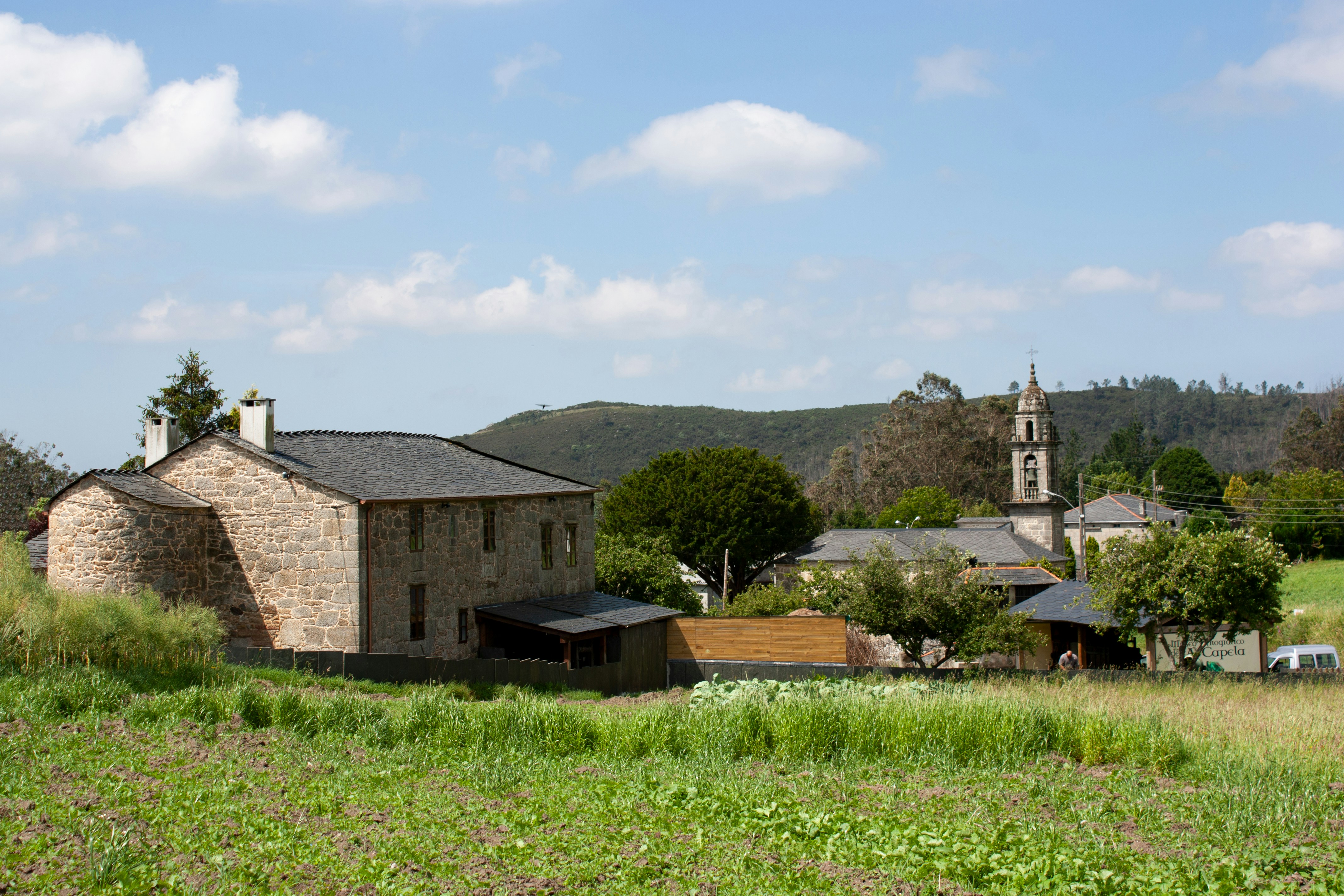 An old stone building in a field with a church in the background