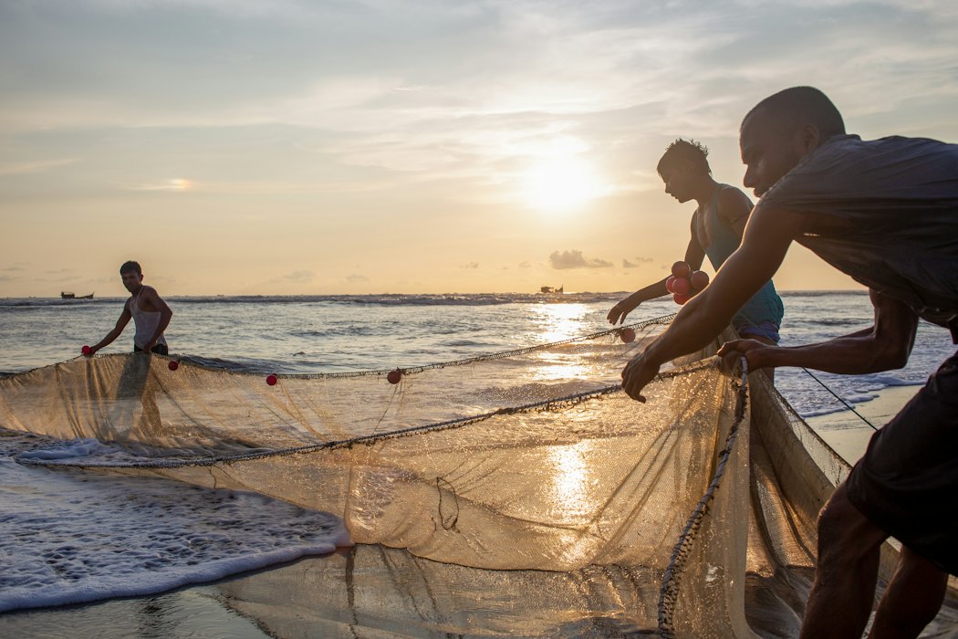 Fishermen pulling nets on the shore at sunrise
