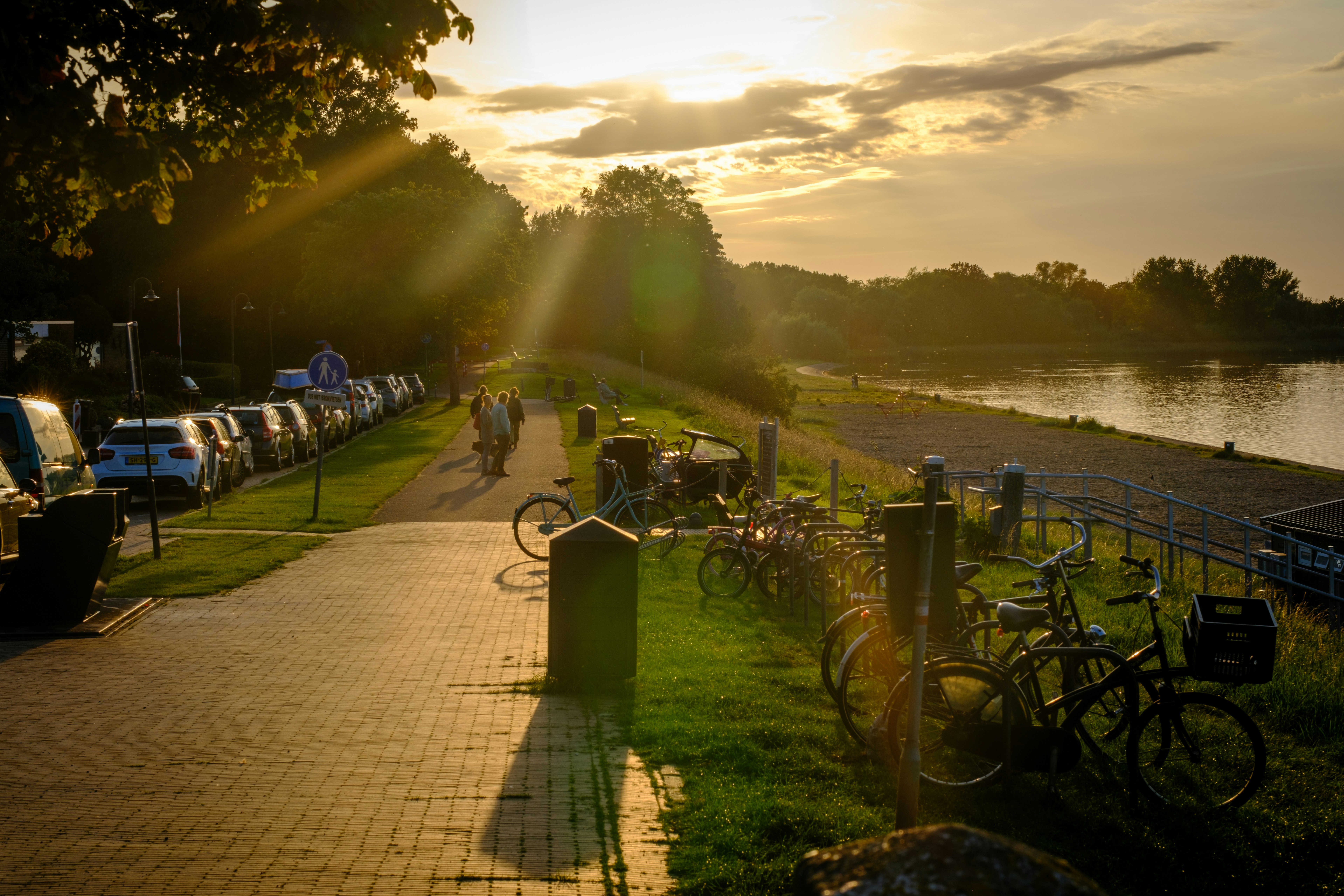 The sun is setting over the water with many bicycles parked on the side of the