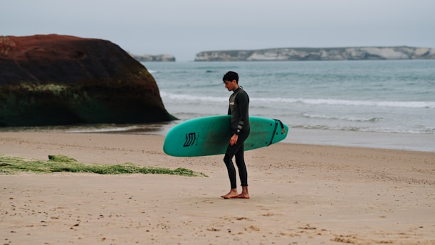 A man standing on a beach holding a surfboard