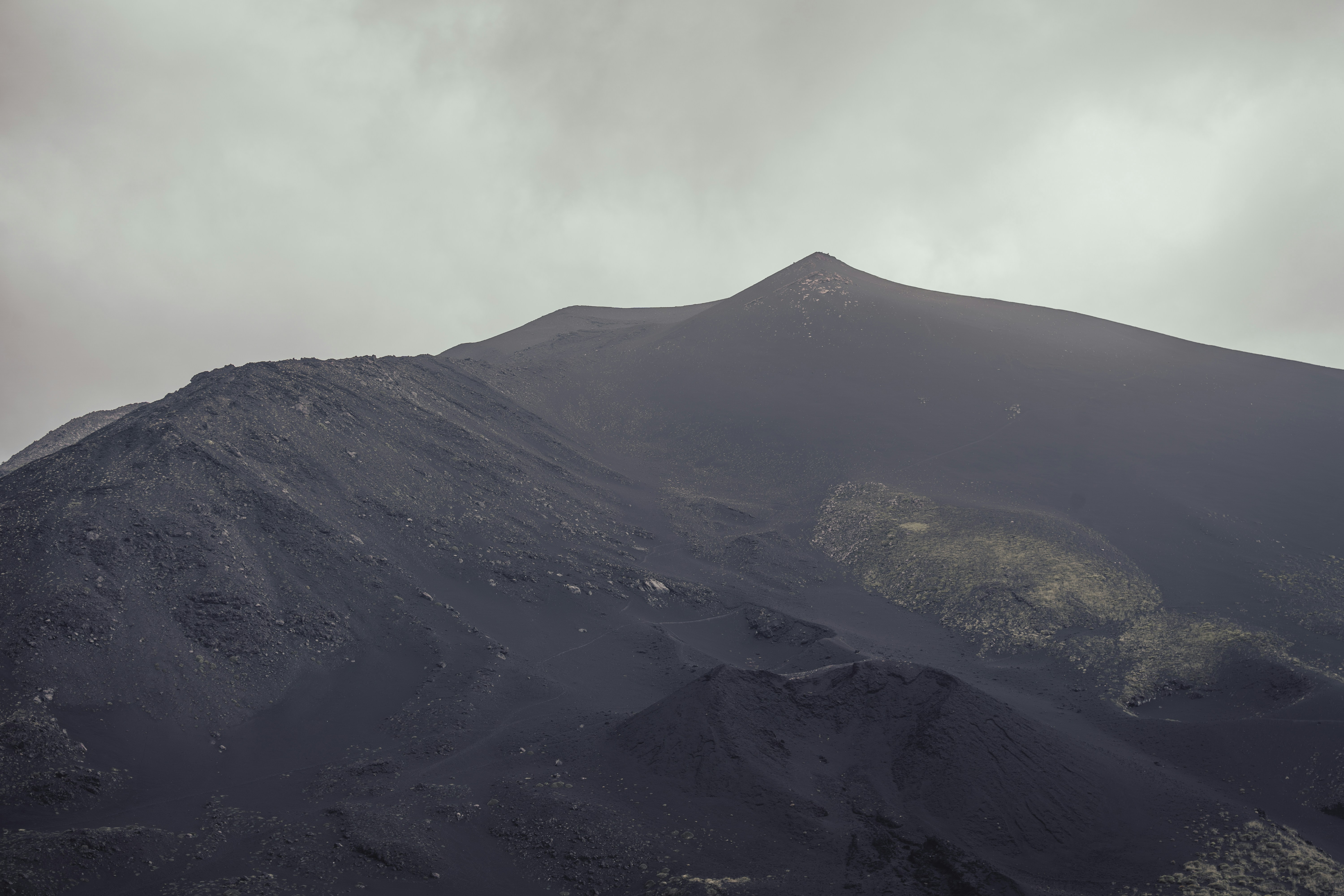 A mountain with a cloudy sky in the background, A view of Mt Etna in the clouds. After an eruption a day prior, the landscape covered with fresh ash and rock.