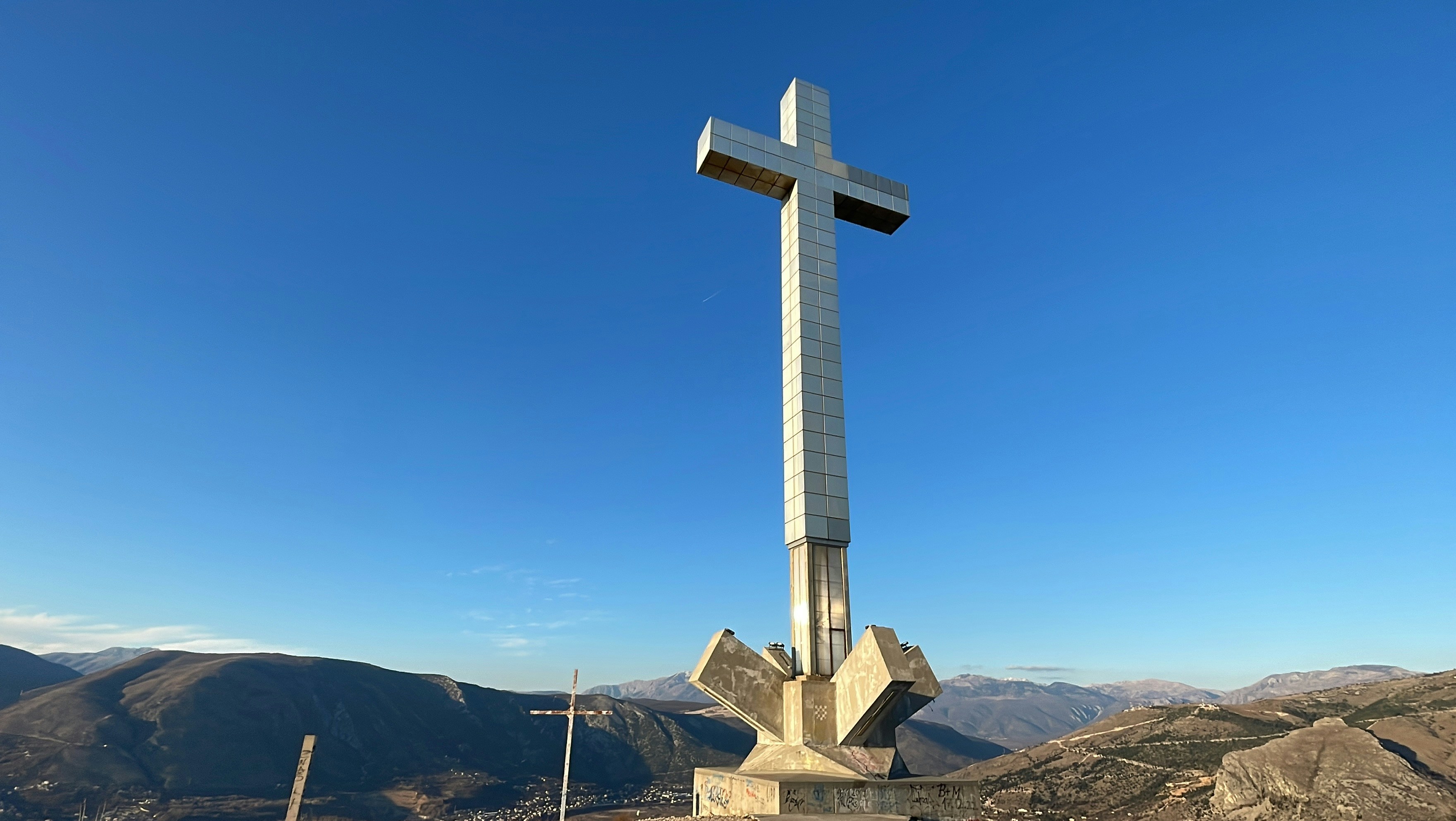 A cross on top of a hill with mountains in the background