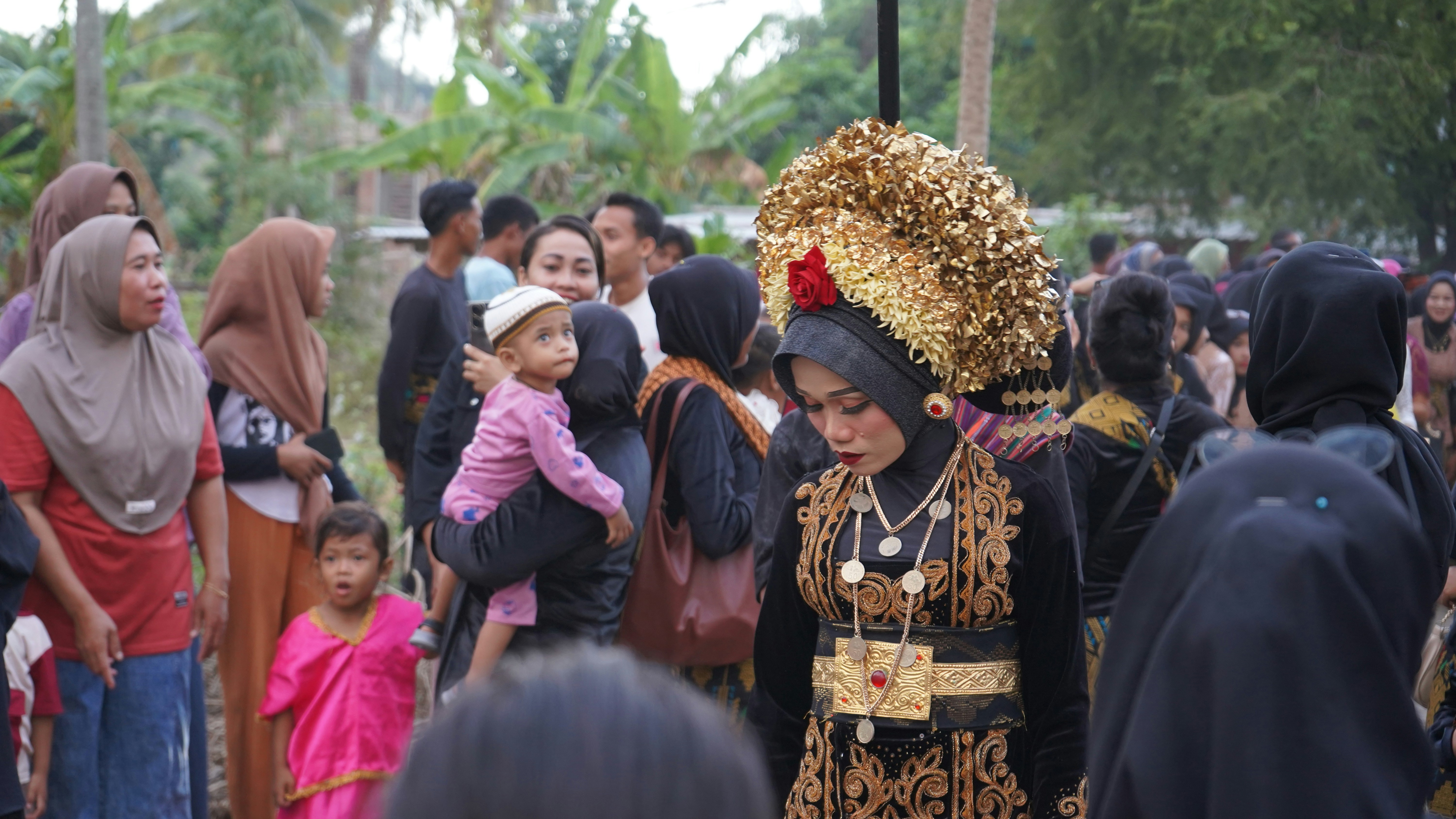 A group of people standing around each other, A stunning bride in traditional Sasak attire, adorned with a gold headdress and intricate designs, at a Lombok wedding.