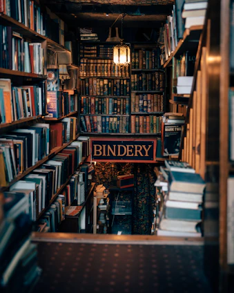 A bookshelf filled with lots of books and a sign that reads bindery