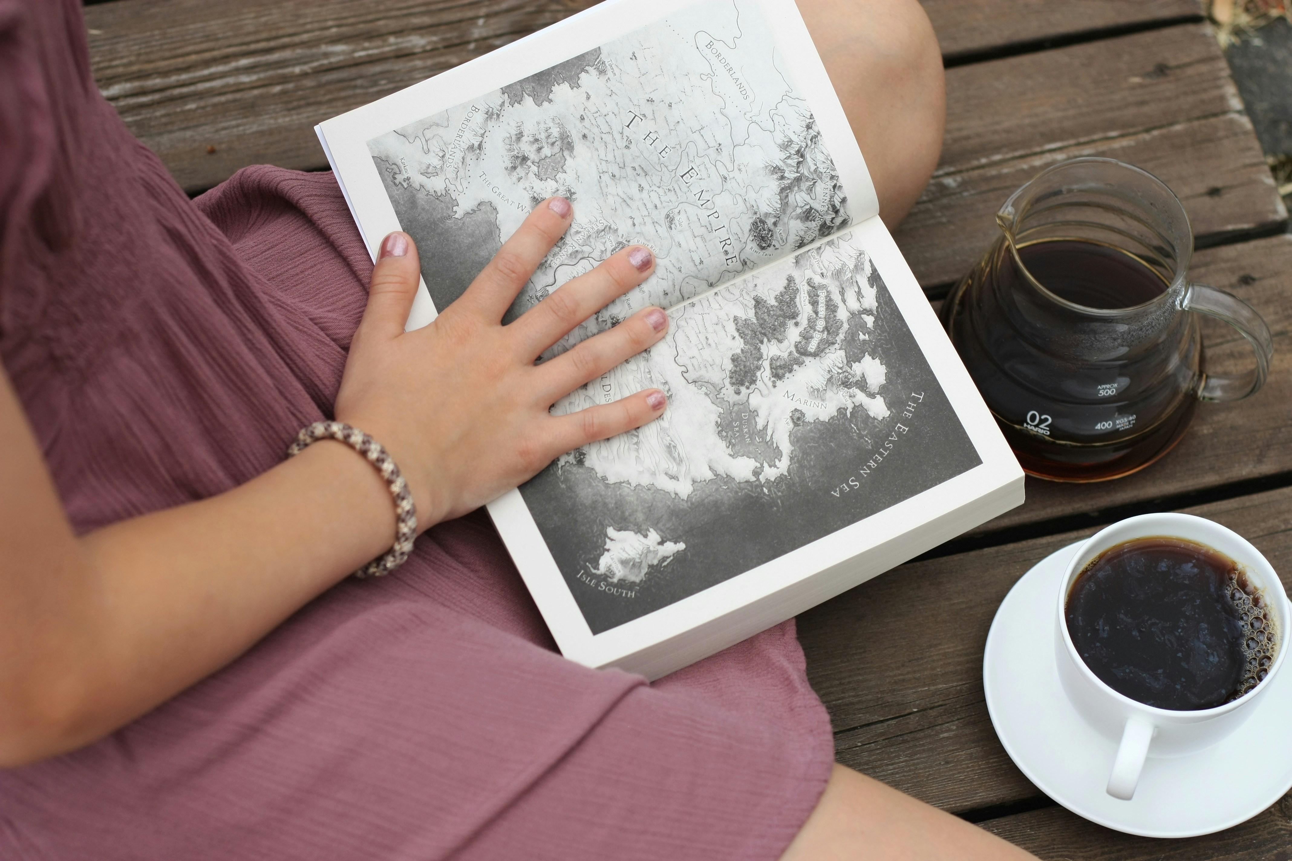 A woman sitting on a bench reading a book next to a cup of coffee
