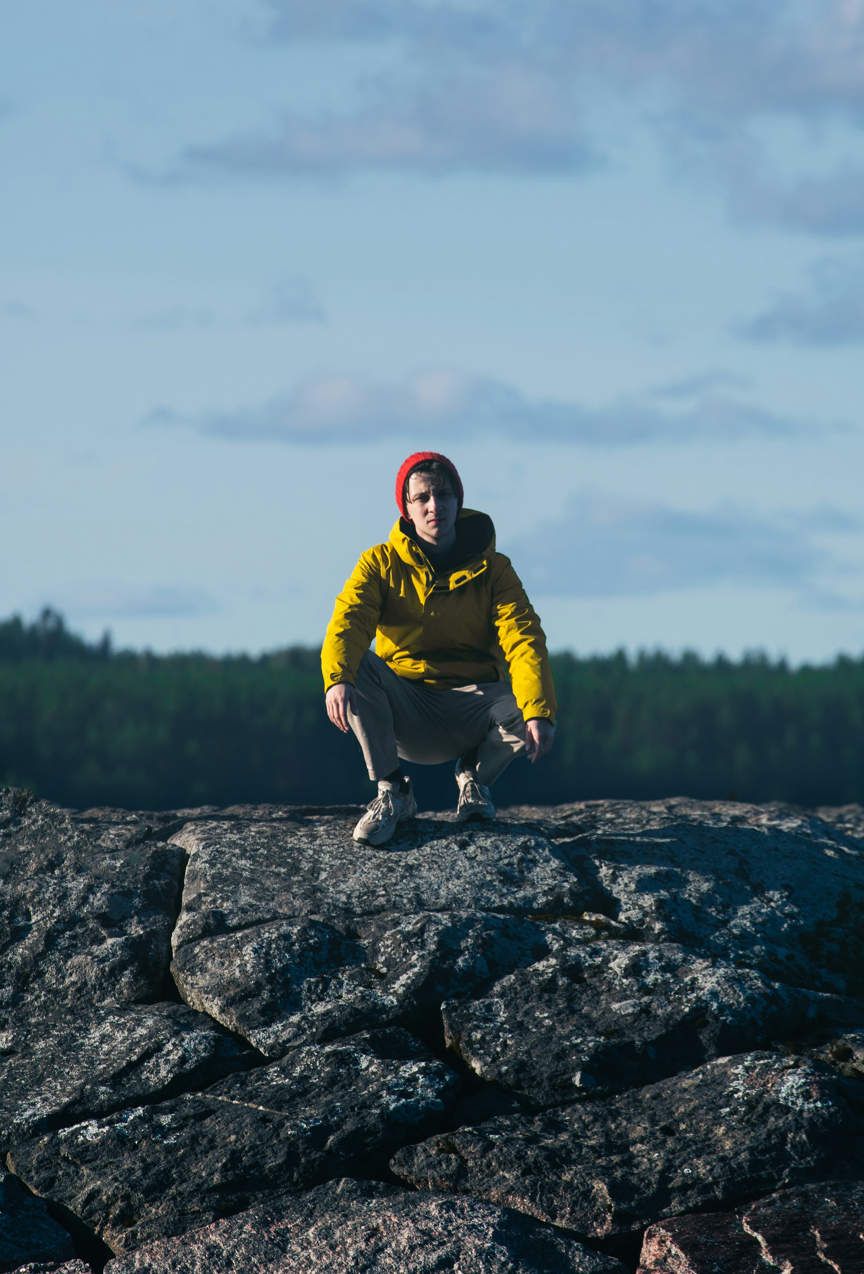 A man in a yellow jacket crouches on a rock photo – Free Hiking Image ...