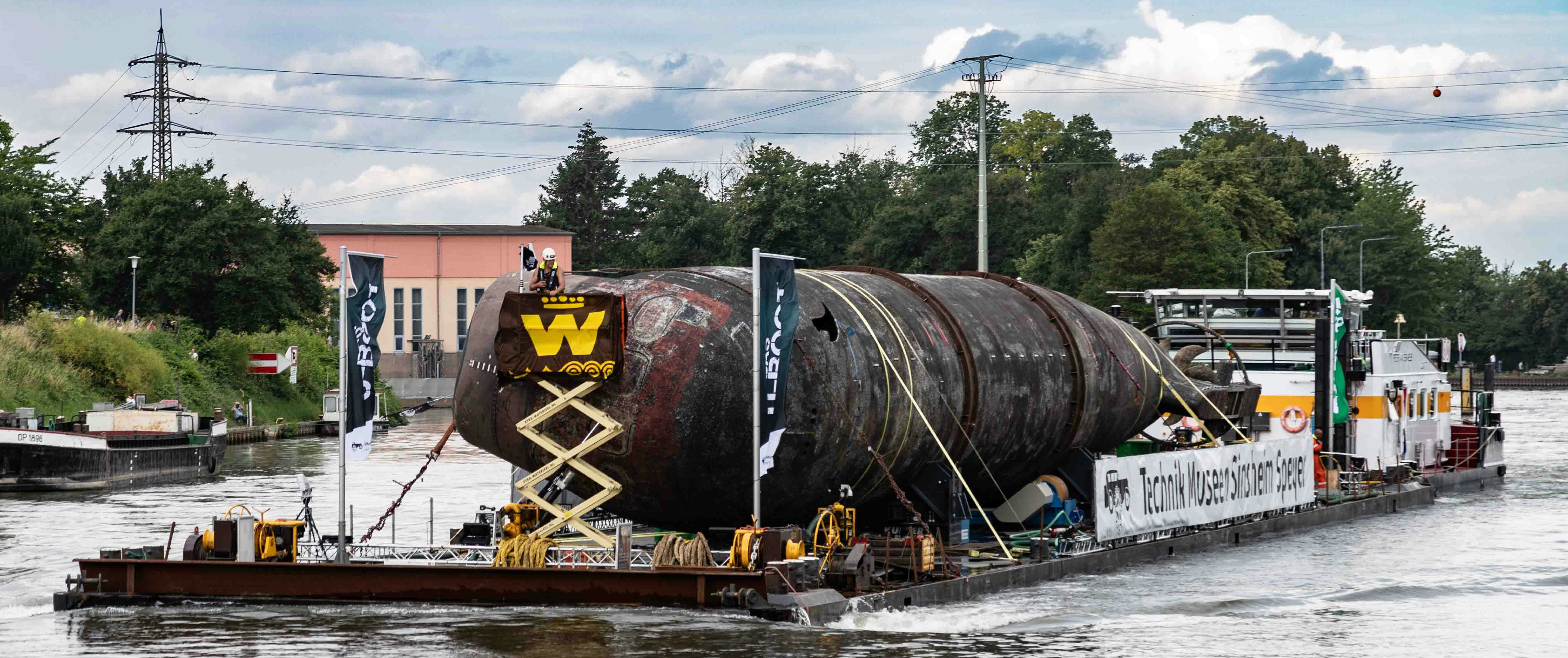 The image shows the U17 submarine being transported on a river barge by the vessel \