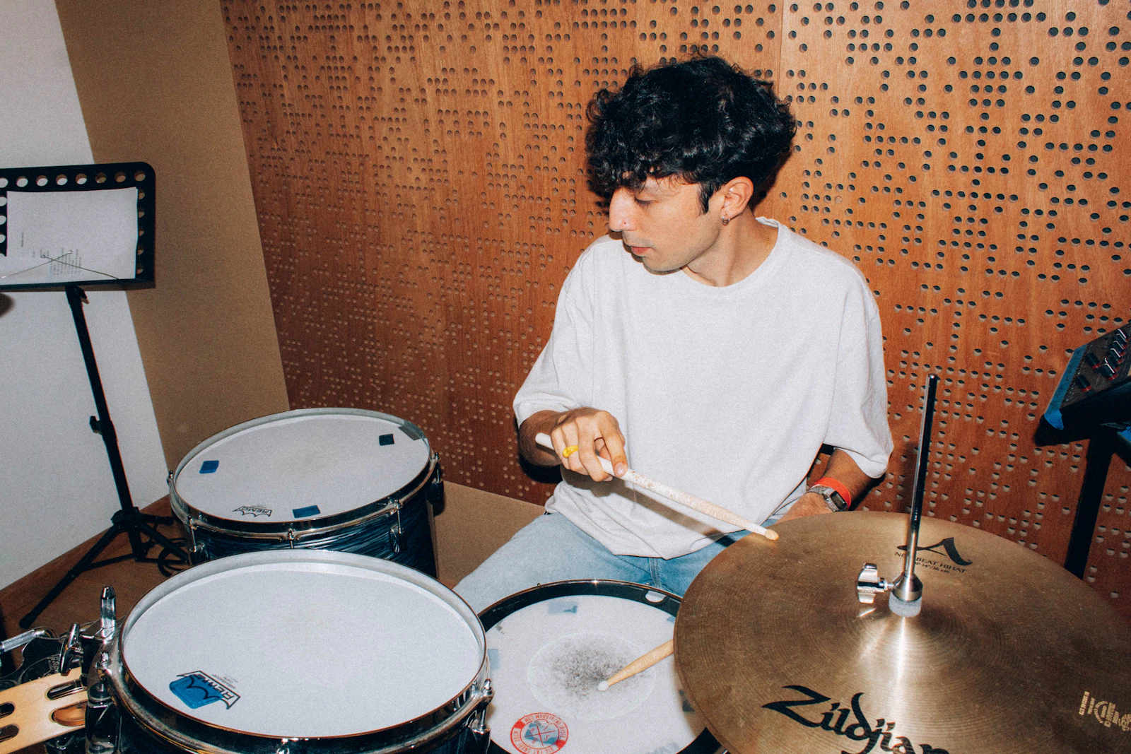 Young man sitting alone in front of a drum set, full attention on the instrument