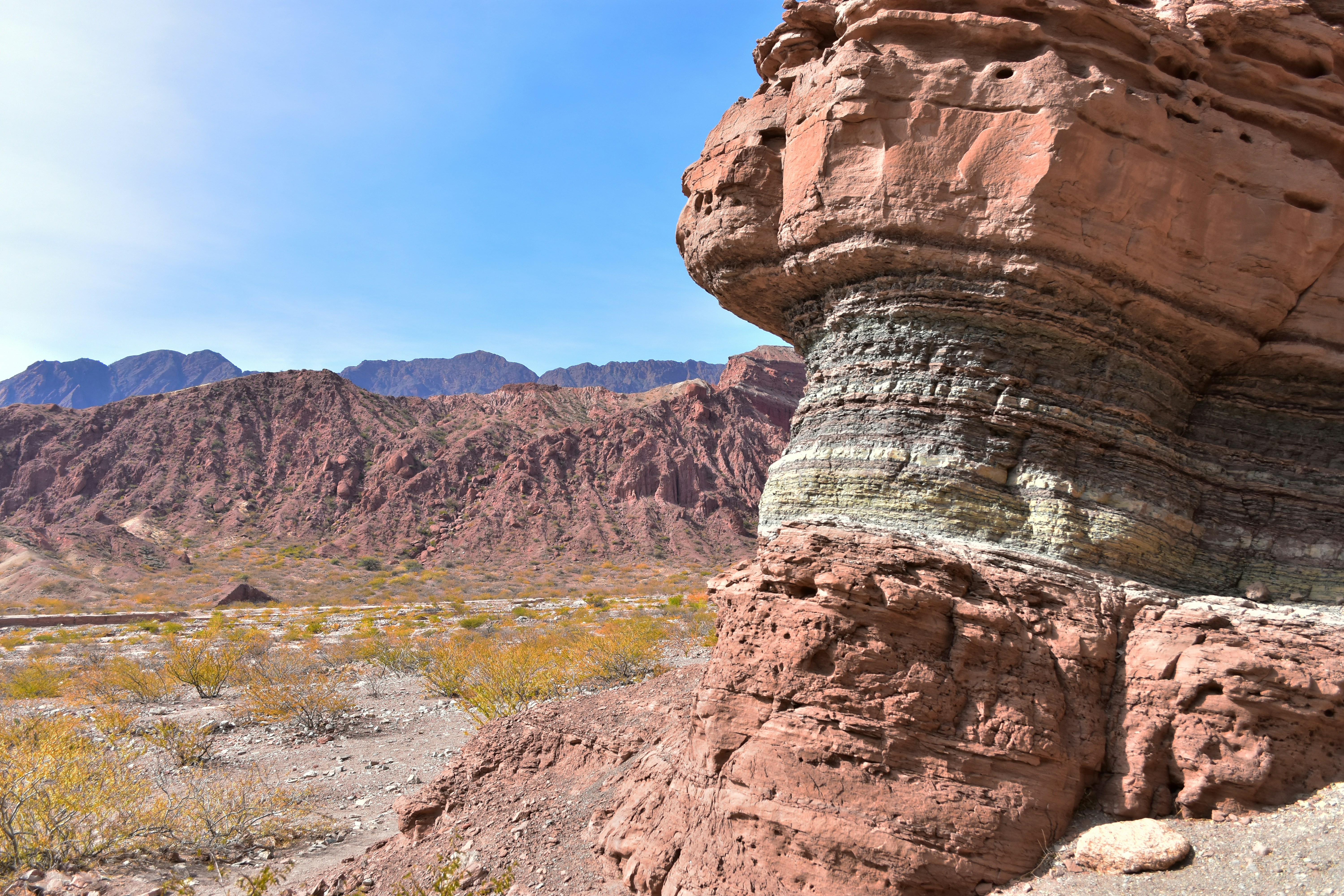 A rock formation in the desert with mountains in the background