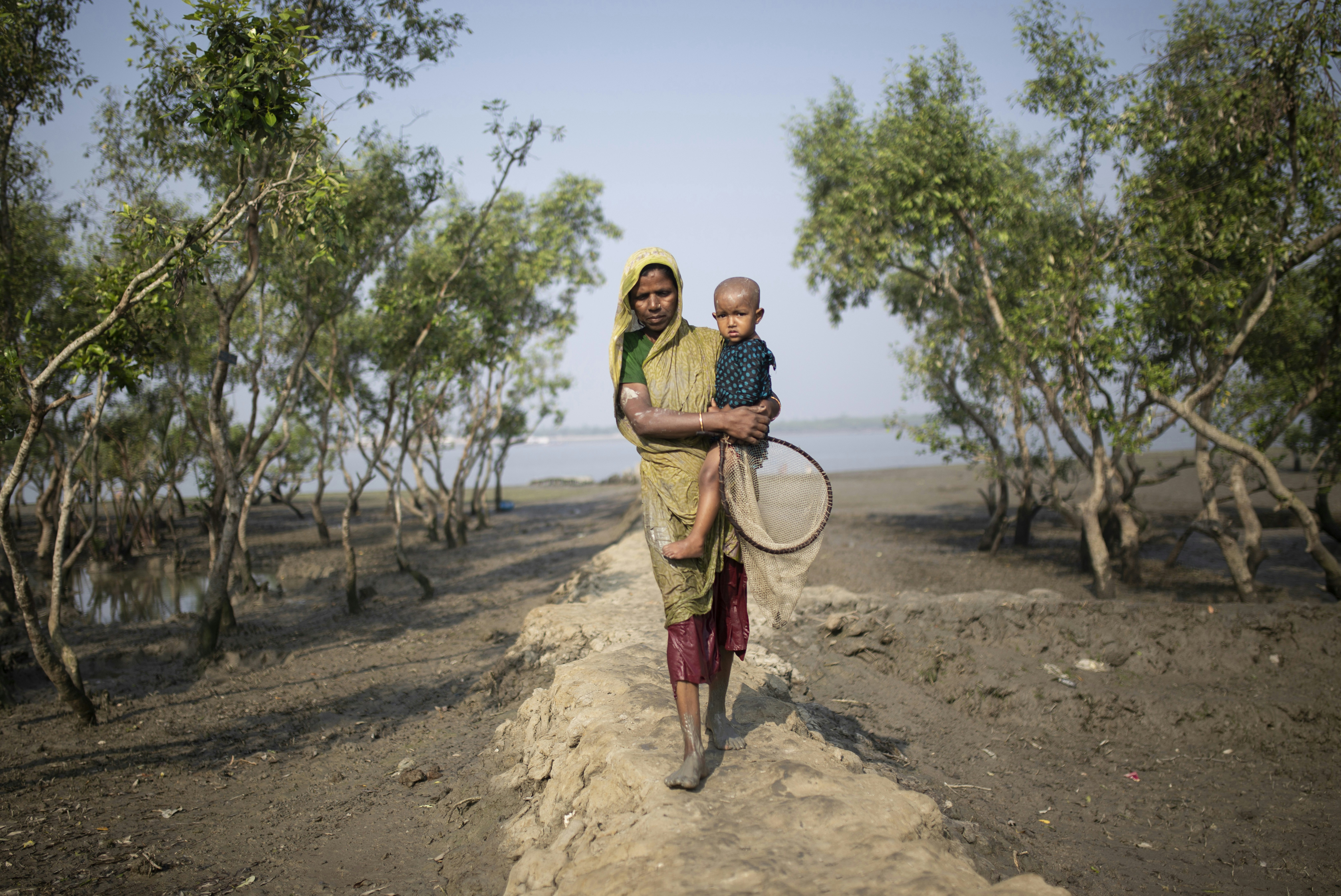 A man carrying a child while walking down a dirt road