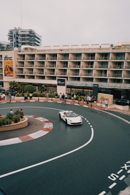 A white car driving down a street next to a tall building