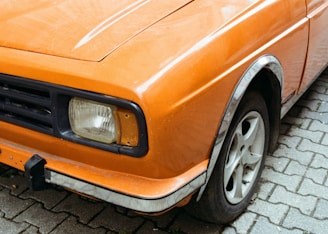 An orange car is parked on a cobblestone street