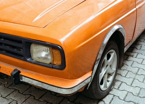 An orange car is parked on a cobblestone street