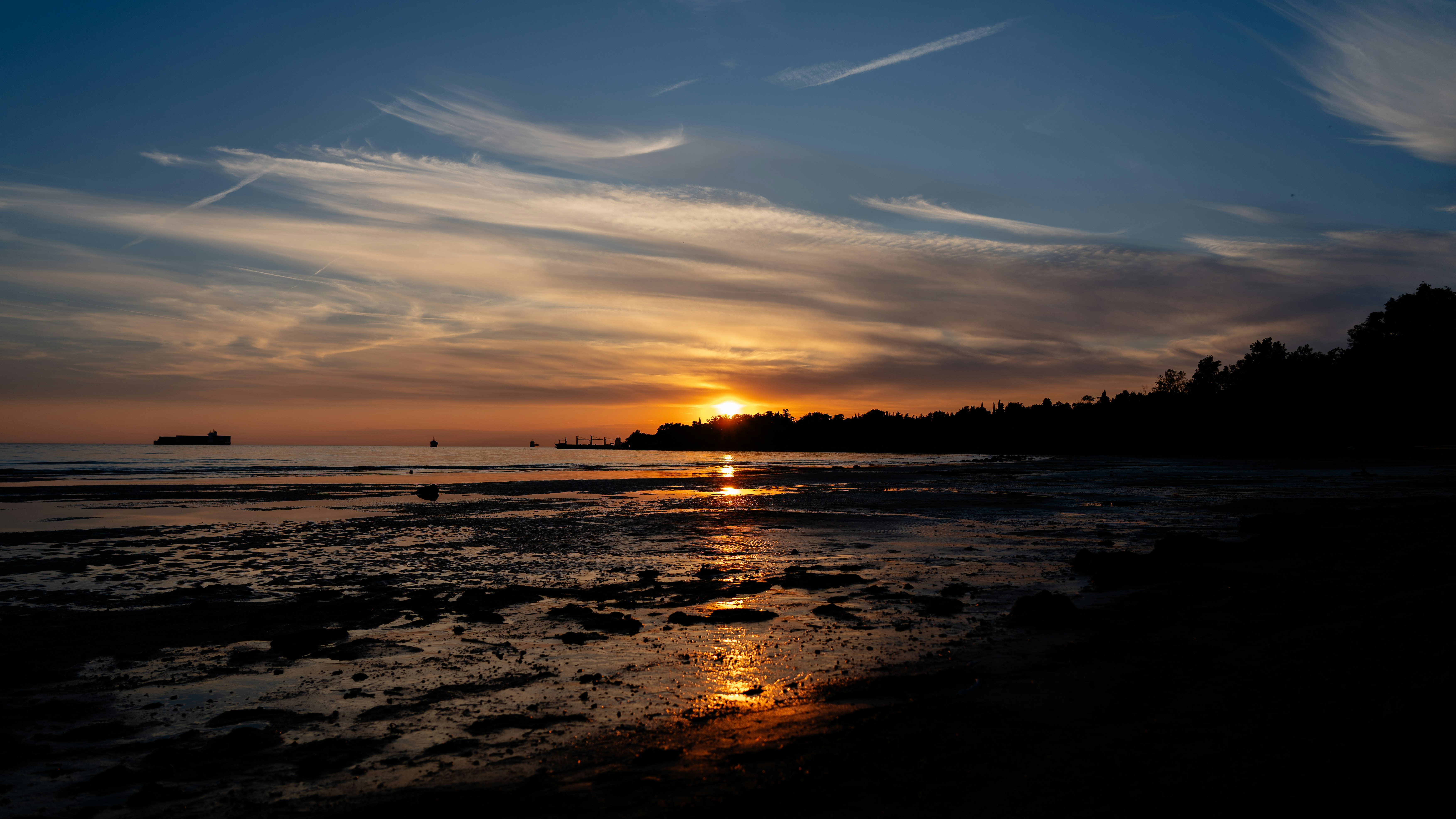 The sun is setting over the water at the beach