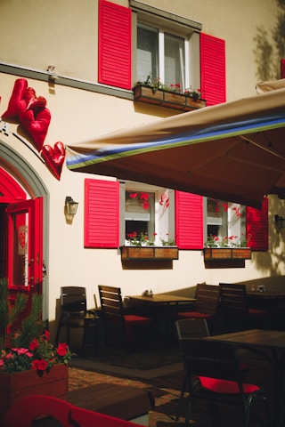 A restaurant with red shutters and tables and chairs