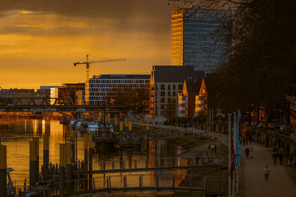 Serene cityscape at sunset with river flowing through it and industrial crane standing tall