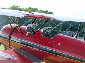 A red airplane parked on top of a lush green field