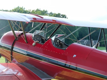 A red airplane parked on top of a lush green field