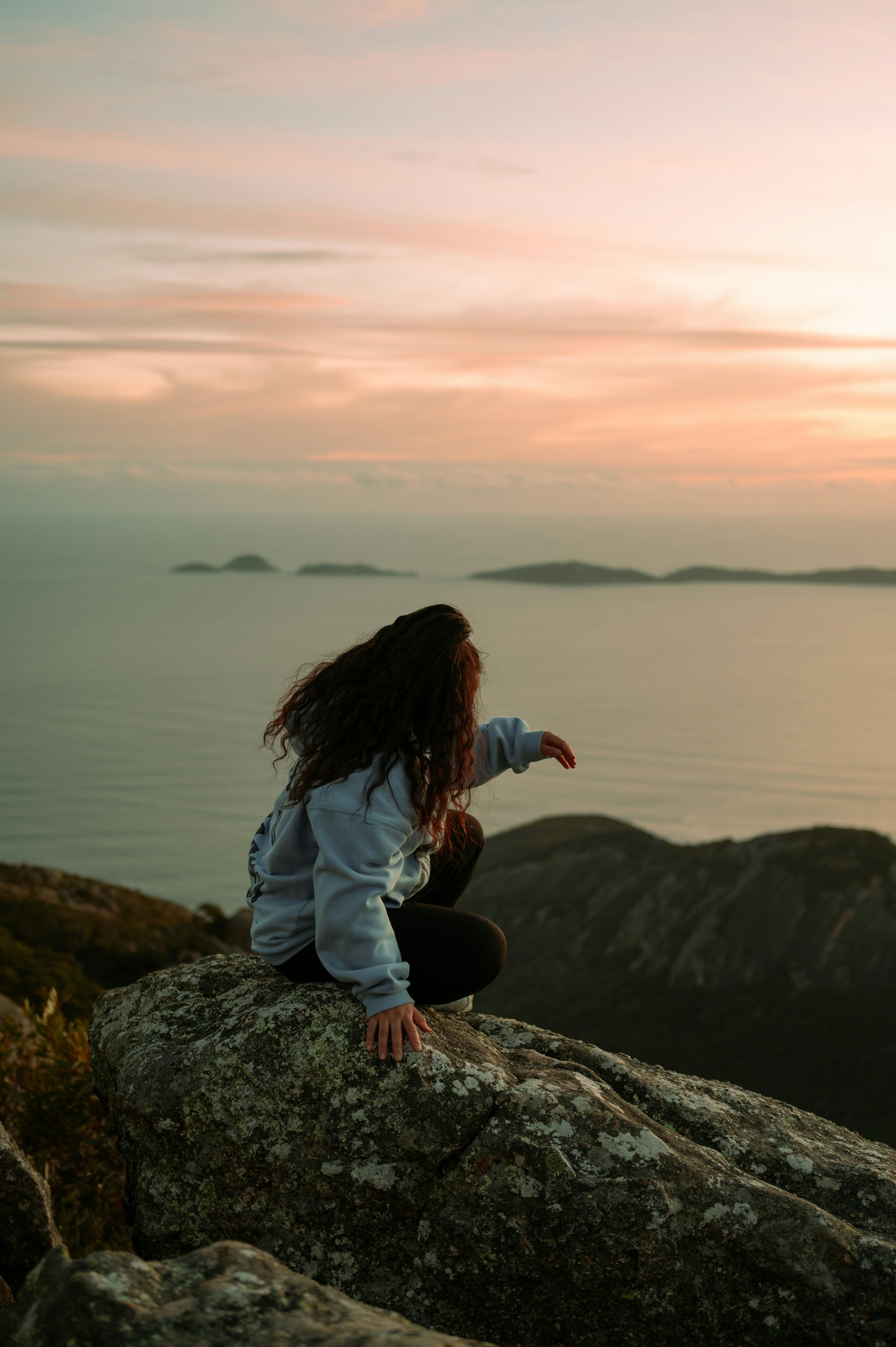 A woman sitting on top of a rock near the ocean