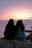 Two women sitting on a rock taking a picture of the sunset