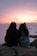 Two women sitting on a rock taking a picture of the sunset