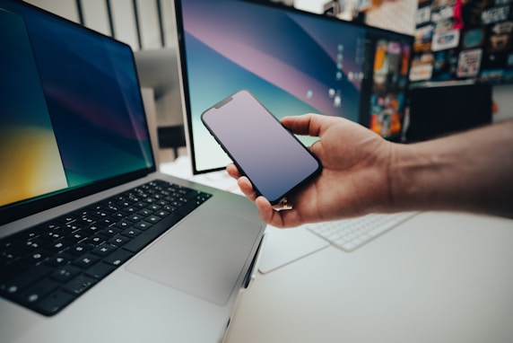 A person holding a cell phone next to a laptop