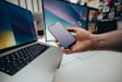 A person holding a cell phone next to a laptop