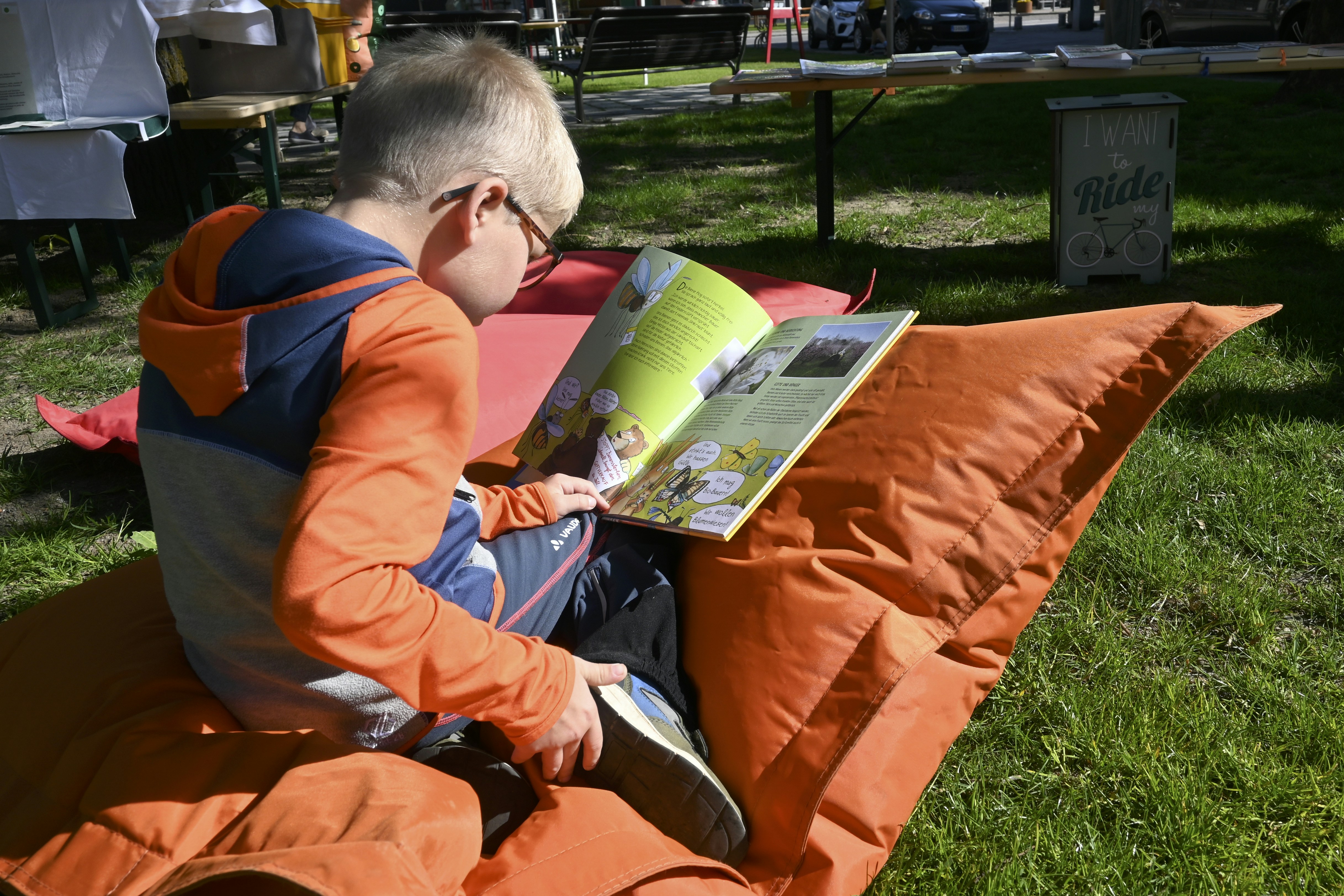 A young boy reading a book while sitting on an orange pillow