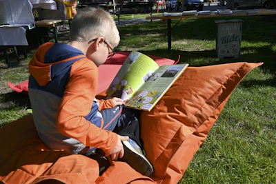 A young boy reading a book while sitting on an orange pillow