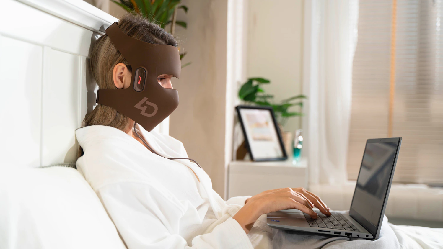 Woman using an LED light therapy mask while working on a laptop