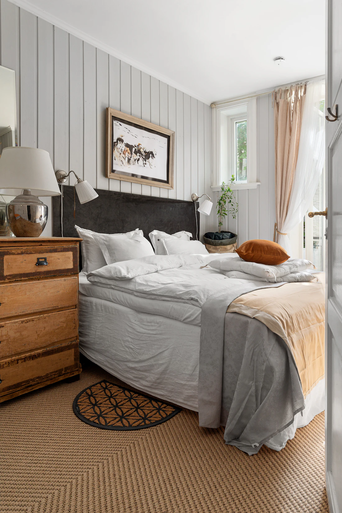 Furnished private bedroom with a made bed, wooden dresser and mirror.