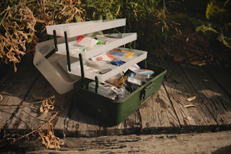 A green suitcase filled with assorted items sitting on a wooden floor