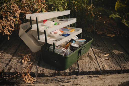 A green suitcase filled with assorted items sitting on a wooden floor