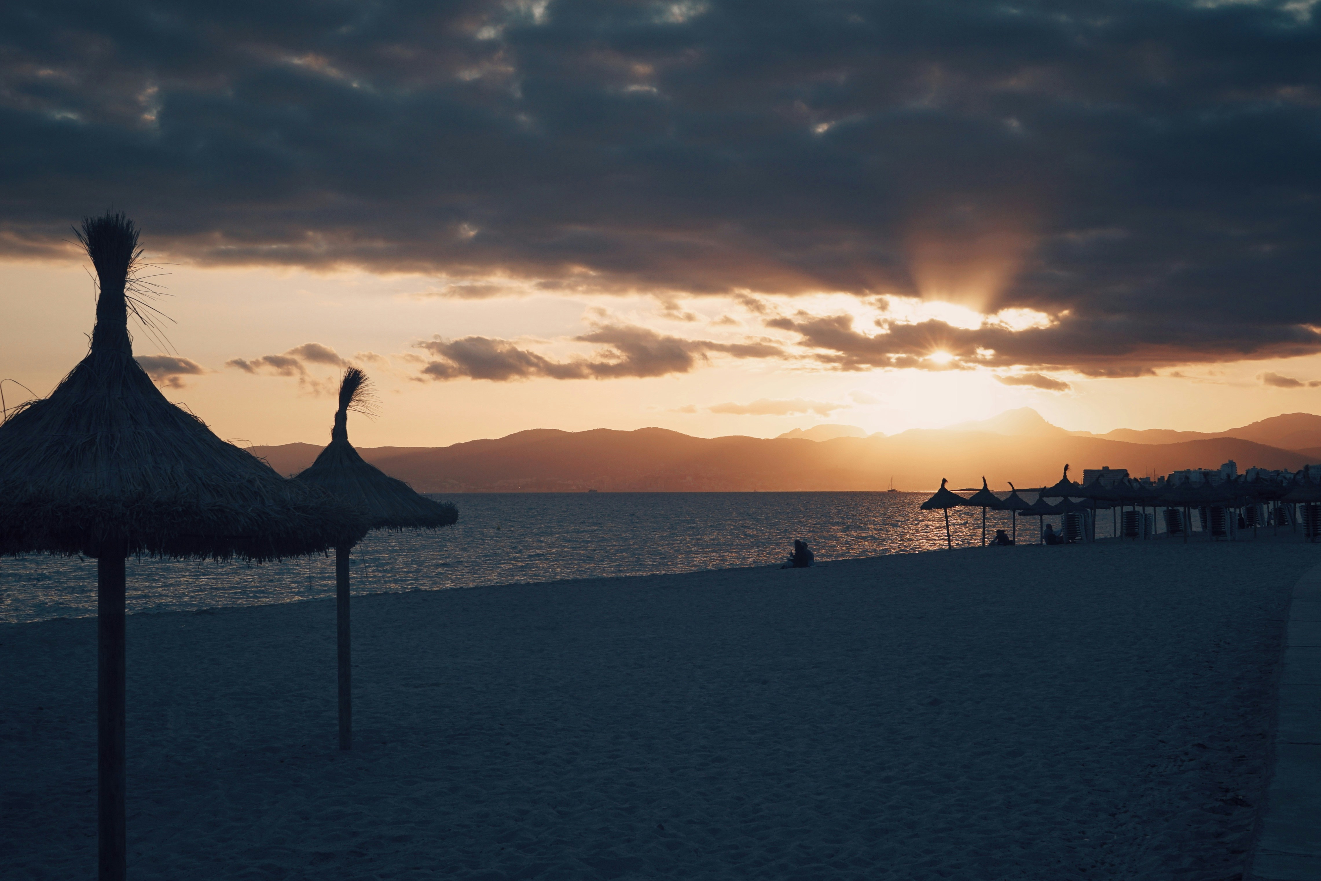The sun is setting on a beach with umbrellas