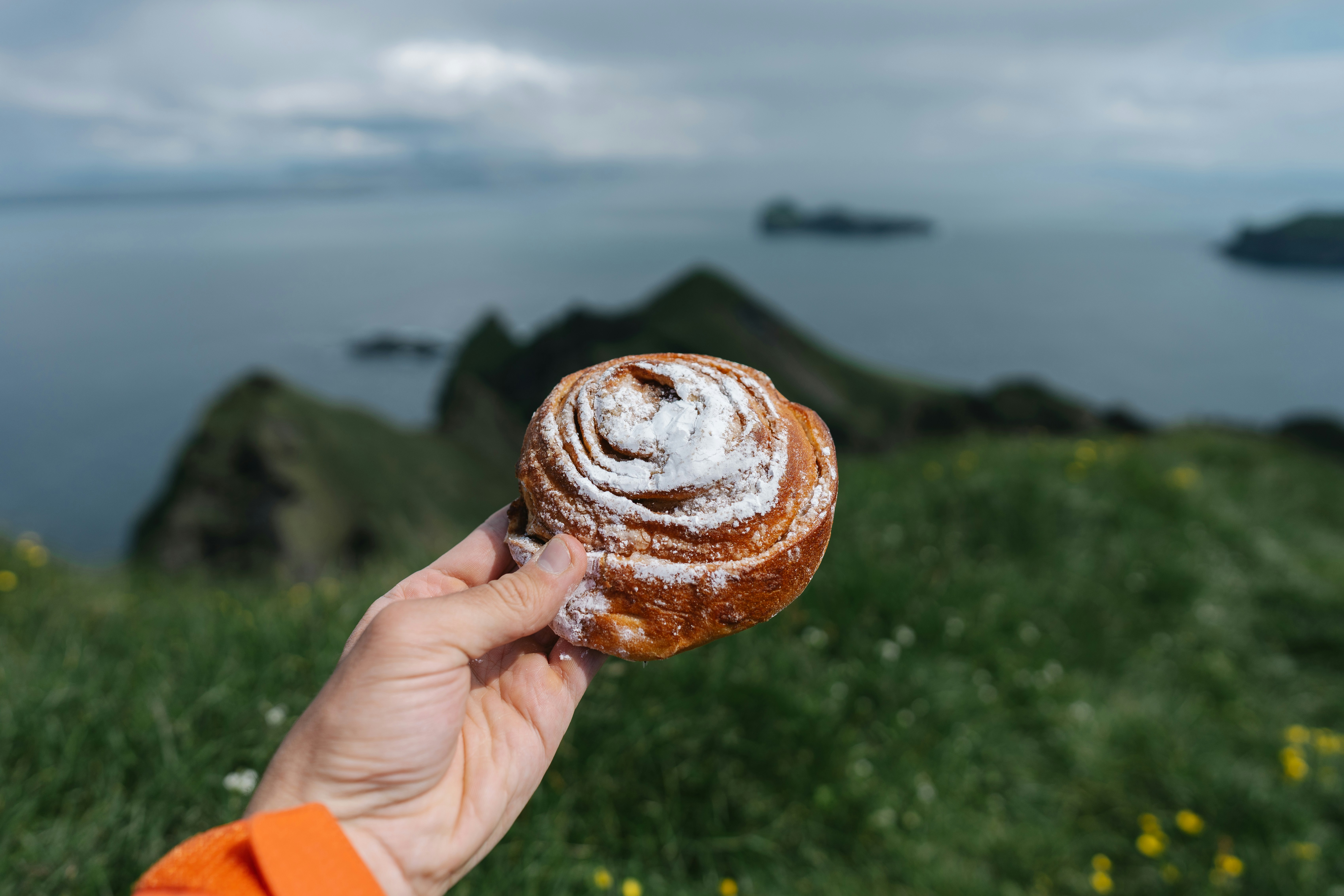 A person holding up a pastry in front of a body of water, 