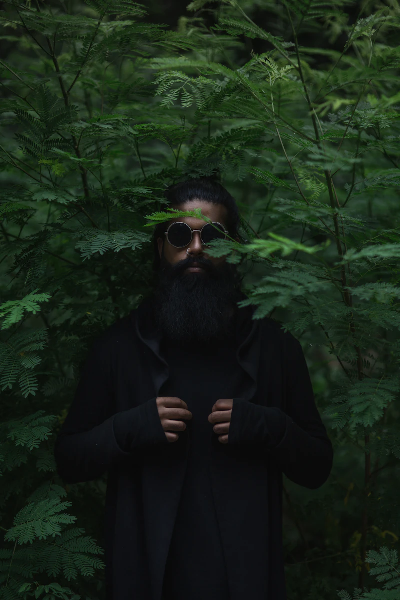 Man with a long beard and sunglasses standing in a forest