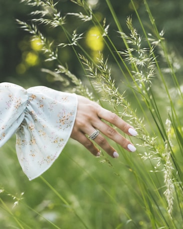 A woman's hand reaching for a flower in a field