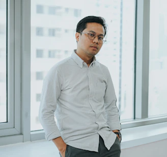 A man standing in front of a window with his hands in his pockets