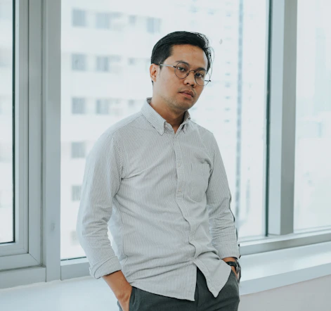 A man standing in front of a window with his hands in his pockets