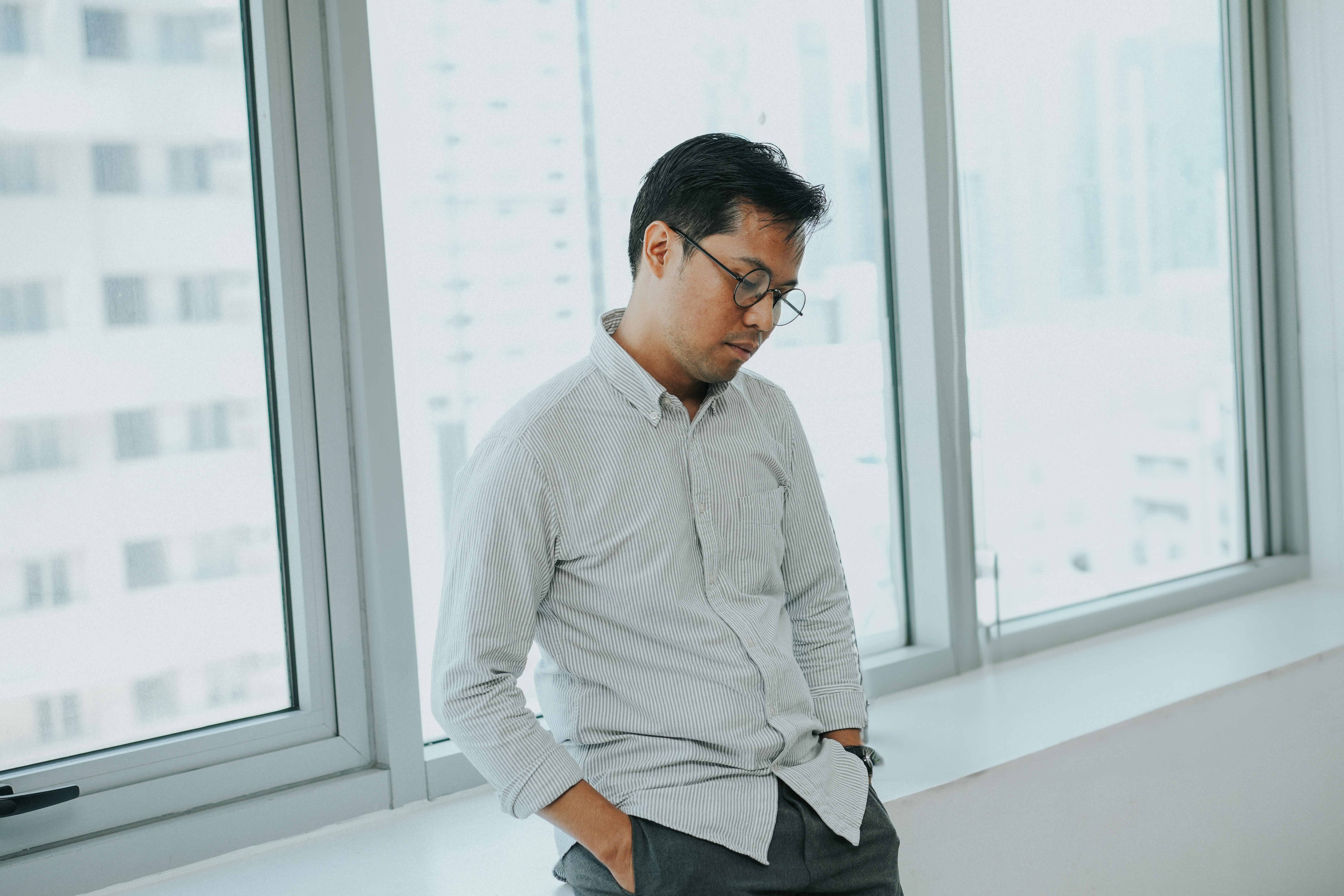 A man standing in front of a window with his hands in his pockets