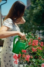 A woman watering flowers with a green watering can