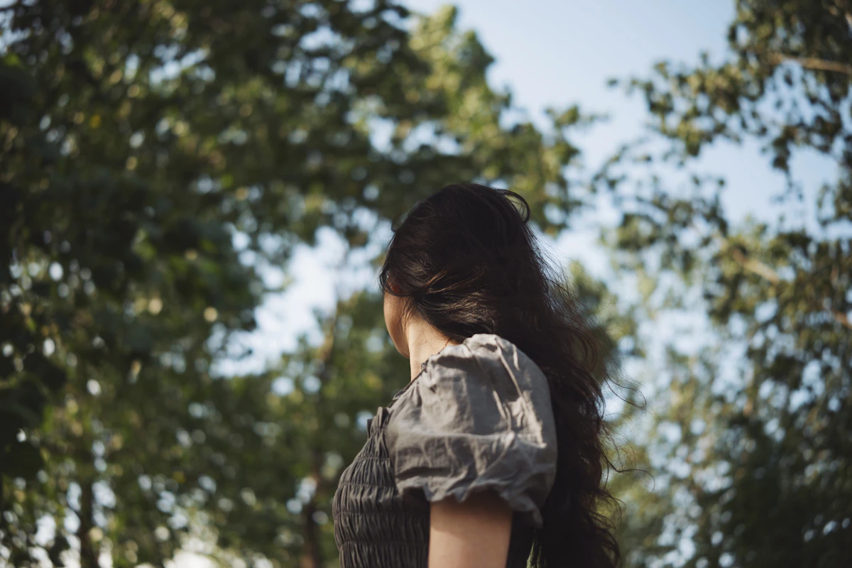 Adult woman from behind looking up at trees in soft daylight
