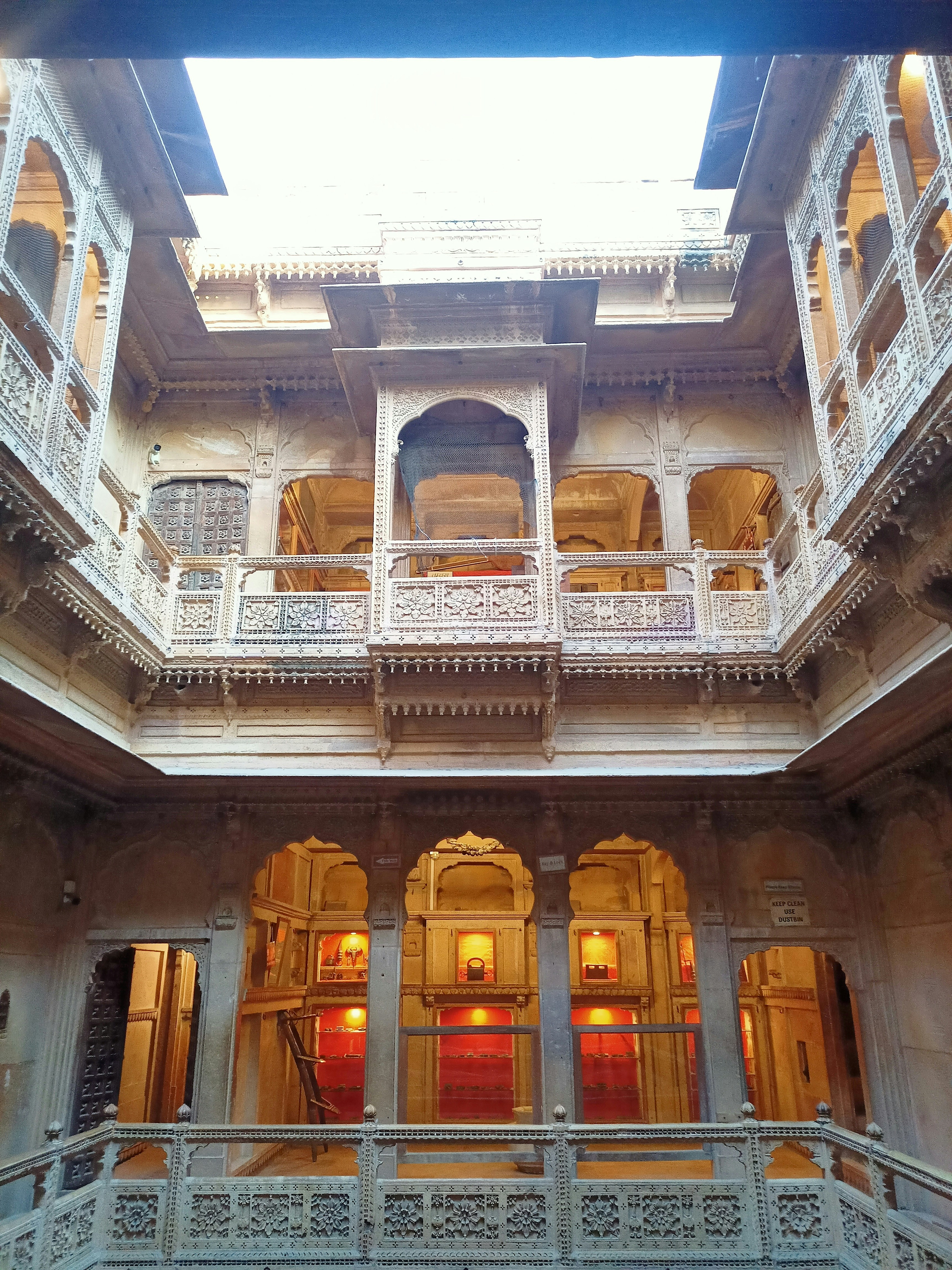 Intricate jharokha stone balconies with floral carvings, overhanging over a narrow palace courtyard, warm golden hour light casting deep shadows