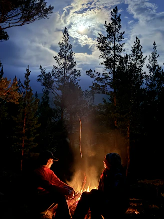 Two people sitting around a campfire at night