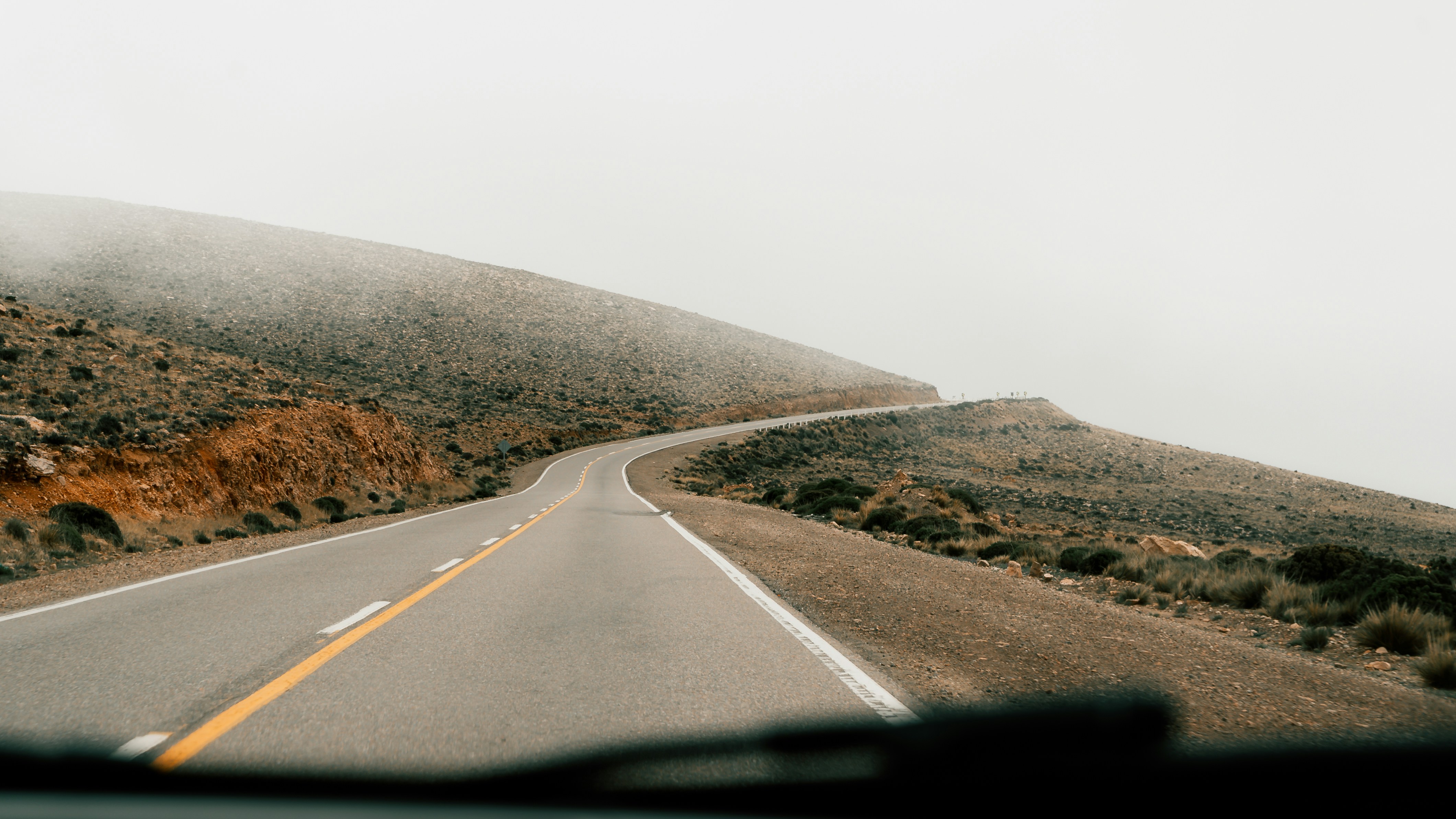A car driving down a road next to a lush green hillside, 