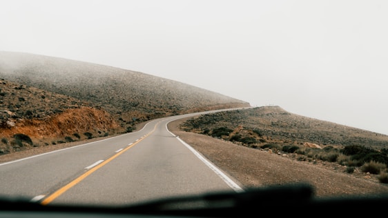 A car driving down a road next to a lush green hillside