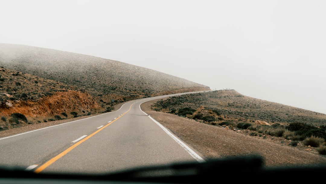 A car driving down a road next to a lush green hillside,